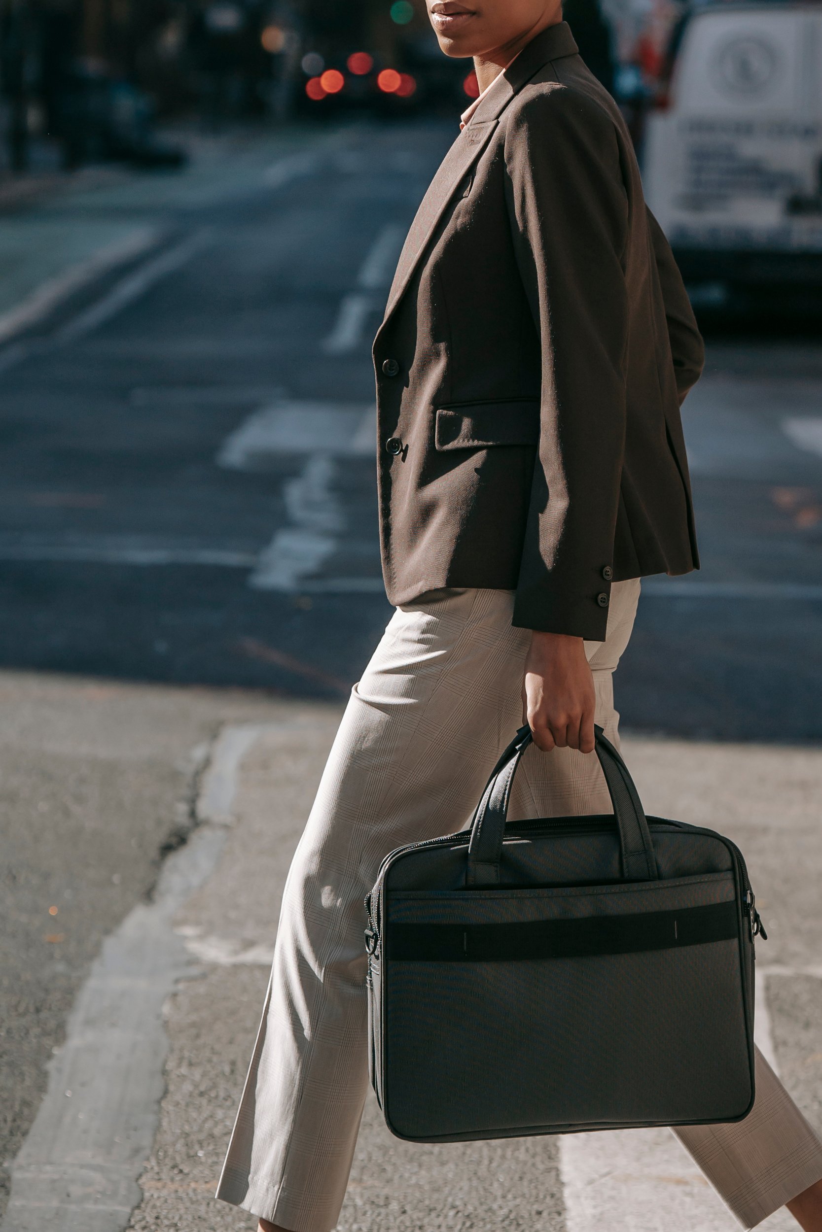 Anonymous elegant ethnic businesswoman with laptop bag walking on zebra crossing